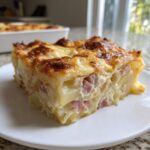 A thick, golden-brown slice of scalloped potatoes and ham baked in a creamy sauce, served on a white plate.