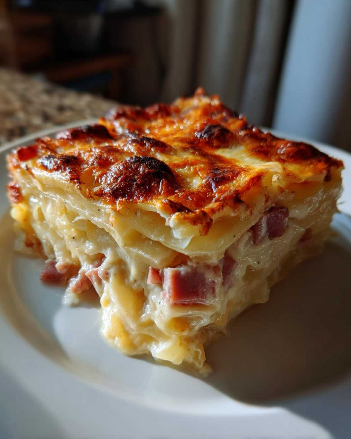 A thick, cheesy slice of scalloped potatoes and ham, showing layers of potato, creamy sauce, and diced ham.