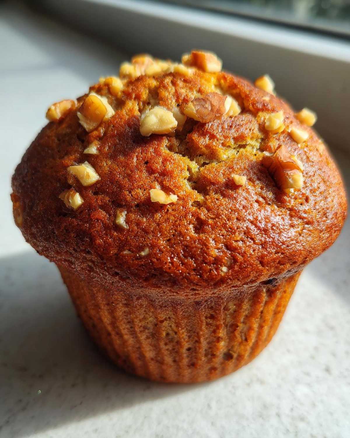 Close-up of a golden brown banana nut muffin, freshly baked and topped with chopped walnuts.