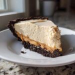 A close-up slice of creamy peanut butter pie featuring a thick, light filling and a dark chocolate cookie crust on a white plate.