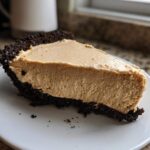 A thick slice of creamy peanut butter pie with a dark chocolate crumb crust resting on a white plate.