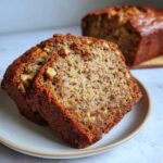 Two thick slices of moist sugar free banana bread with visible walnuts served on a small plate.
