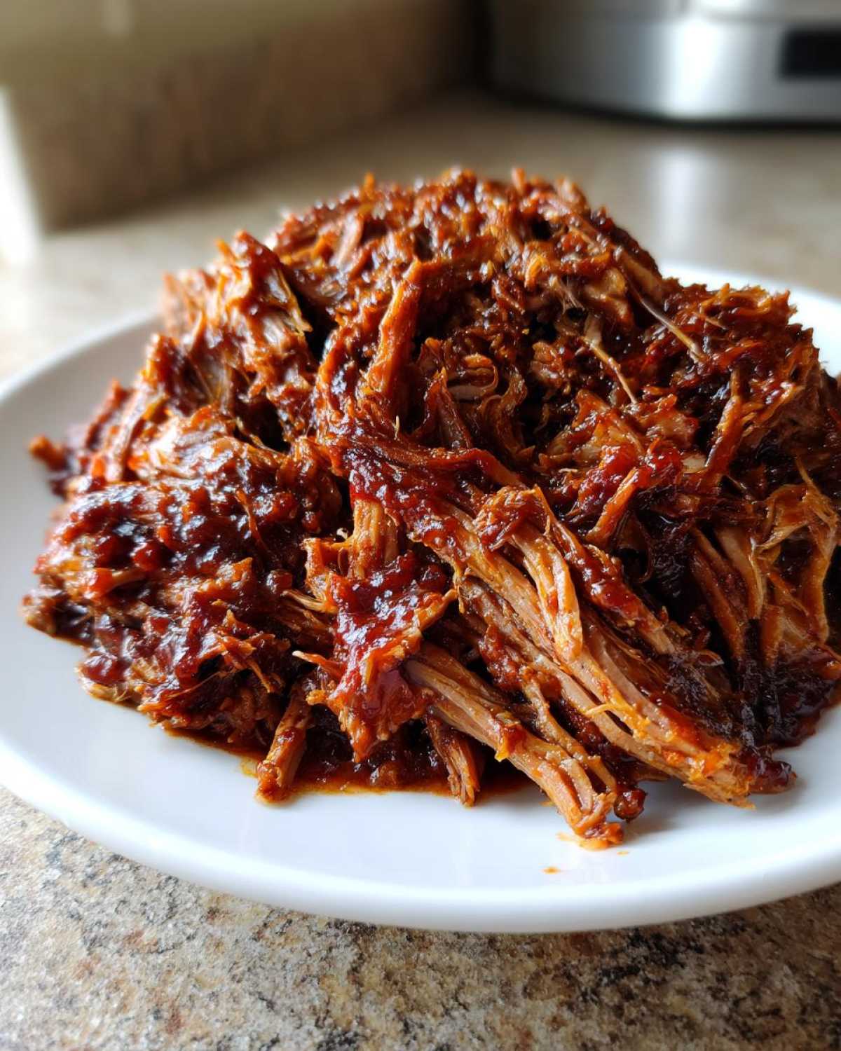 A close-up of shredded, saucy Slow Cooker Pulled Pork piled high on a white plate.