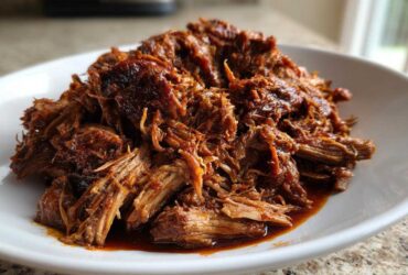 A close-up of tender, shredded Slow Cooker Pulled Pork coated in rich barbecue sauce piled high on a white plate.