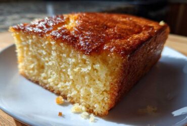 Close-up of a moist, golden slice of sourdough cornbread with a shiny, caramelized top served on a white plate.