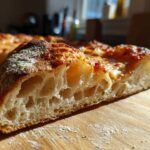 Close-up of a slice of pizza made with sourdough discard pizza dough, showing an airy, open crumb structure.