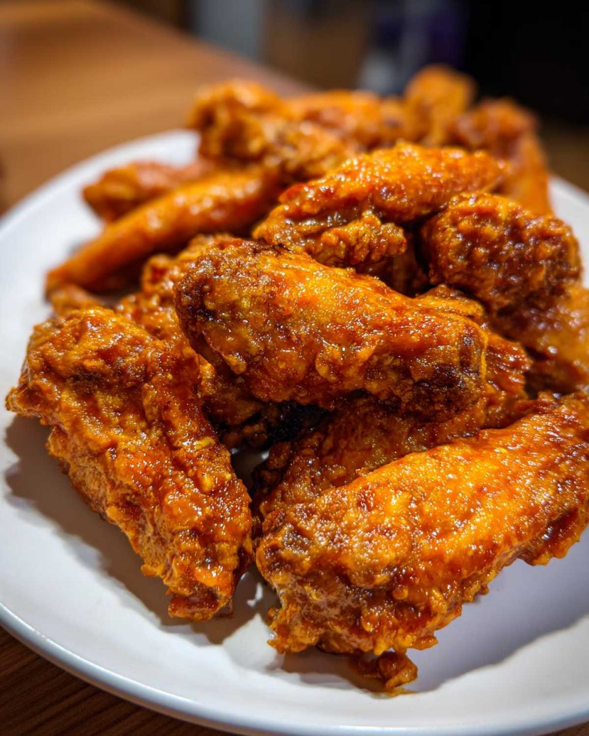 A close-up shot of crispy, glazed chicken wings piled high on a white plate, coated in a vibrant orange sauce.
