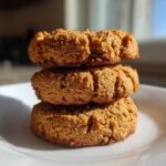 A stack of three golden brown, textured breakfast cookie treats sitting on a white plate.