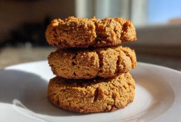 A stack of three golden brown, textured breakfast cookie treats sitting on a white plate.