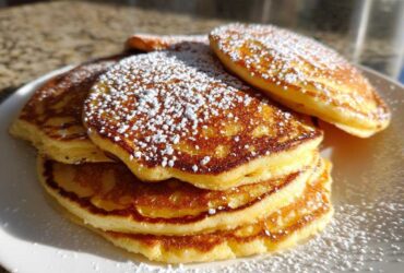 A close-up of a stack of golden brown sourdough pancakes dusted generously with white powdered sugar.