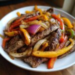 Close-up of perfectly cooked steak fajitas featuring strips of seasoned steak mixed with colorful sautéed bell peppers and onions.