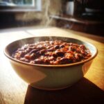 A steaming bowl of rich, hearty chili, featuring kidney beans and meat sauce, ready to eat.