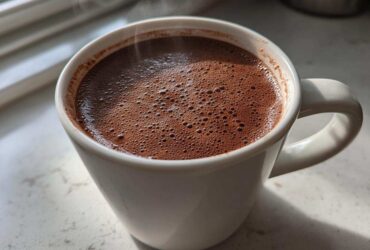 Close-up of a steaming white mug filled with rich, dark brown hot cocoa mix, bubbling slightly.