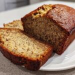 A close-up of a golden brown sugar free banana bread loaf with two slices cut and resting on a white plate.