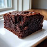 A close-up of a moist, dark chocolate sweet potato brownies square served on a white plate.