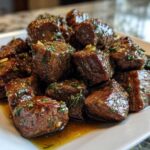 Close-up of tender, glazed crockpot steak bites seasoned with herbs and garlic on a white plate.
