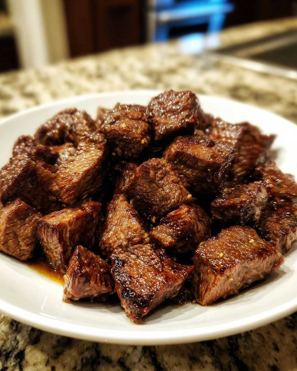 A white plate piled high with tender, browned cubes of crockpot steak glistening with sauce.