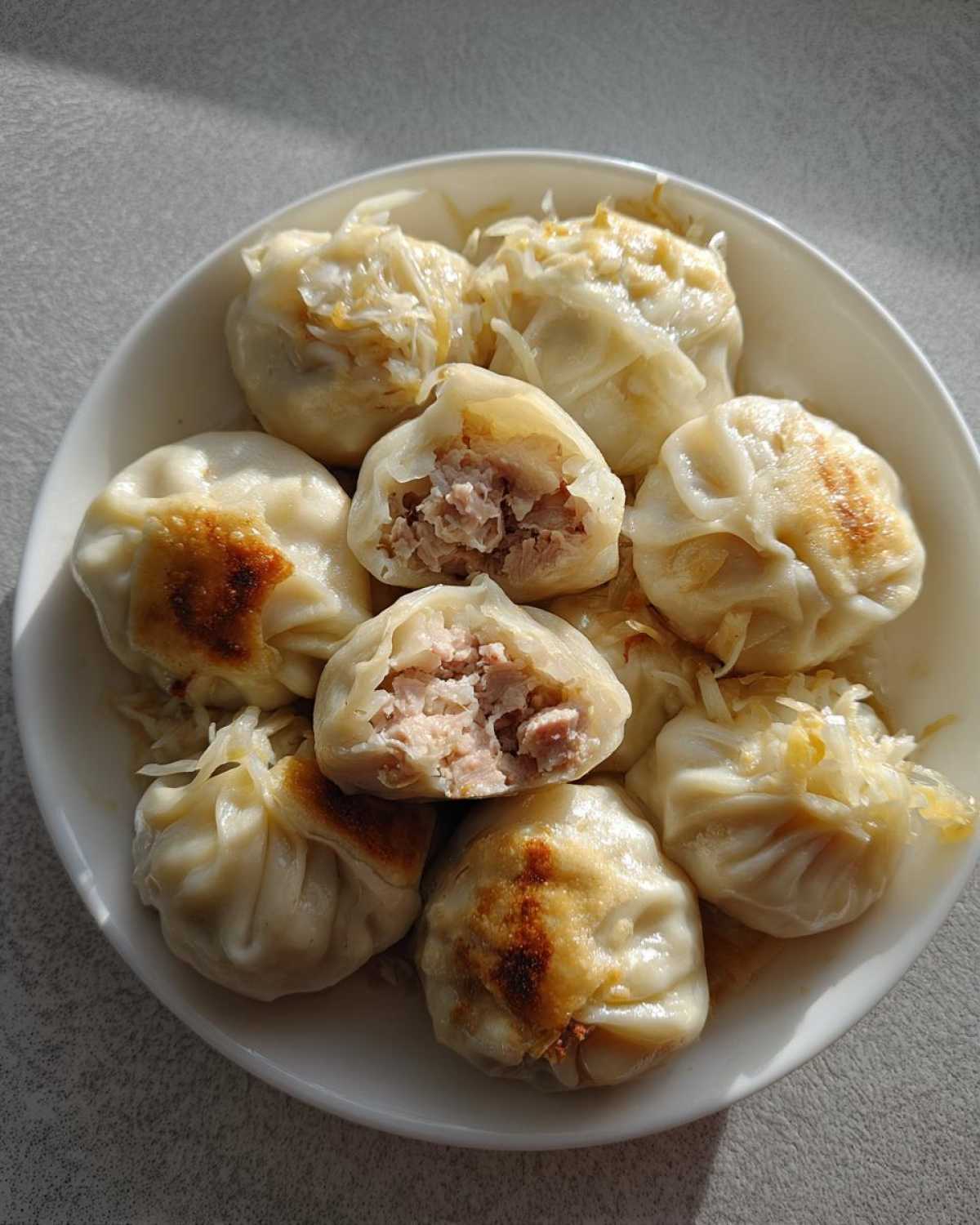 A white plate filled with pan-fried Traditional Chinese Dumplings, one cut open to show the savory meat filling.