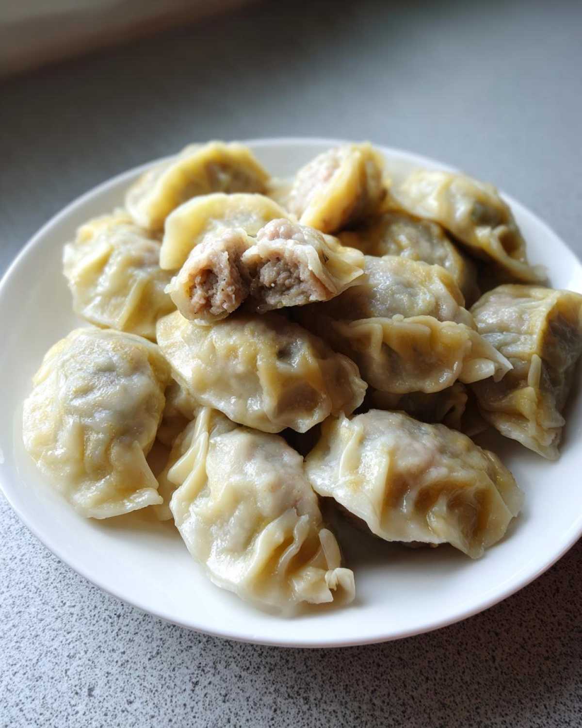 A plate of freshly steamed Traditional Chinese Dumplings, one cut open to show the savory meat filling.