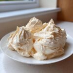 Close-up of fluffy swirls of homemade vanilla buttercream frosting piled high on a white plate.