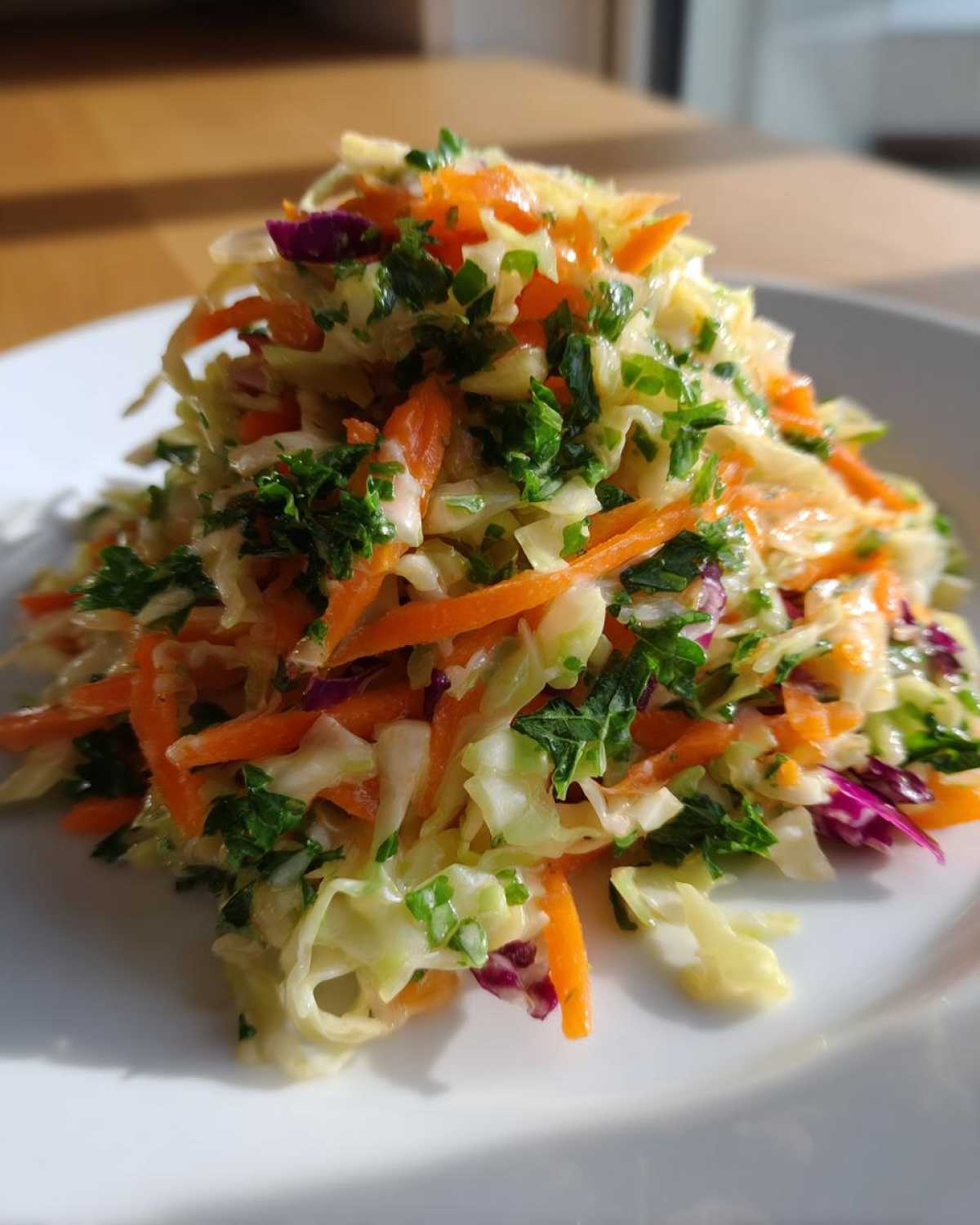Close-up of a vibrant, healthy cabbage salad featuring shredded carrots, green cabbage, and fresh parsley.