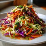 A close-up of a vibrant, healthy cabbage salad featuring shredded green and red cabbage, bright orange carrots, and fresh parsley.