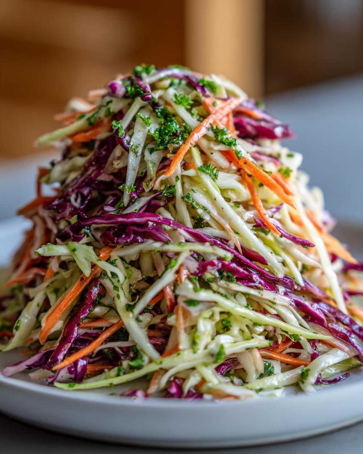 A tall mound of colorful shredded cabbage salad featuring green, red cabbage, and shredded carrots, topped with fresh parsley.