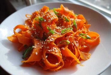 Close-up of a vibrant raw carrot salad made with shaved carrot ribbons, topped with sesame seeds and green onions.