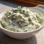 Close-up of thick 5-Minute Greek Yogurt Ranch Dip, creamy white with visible green herbs like dill, served in a white bowl.