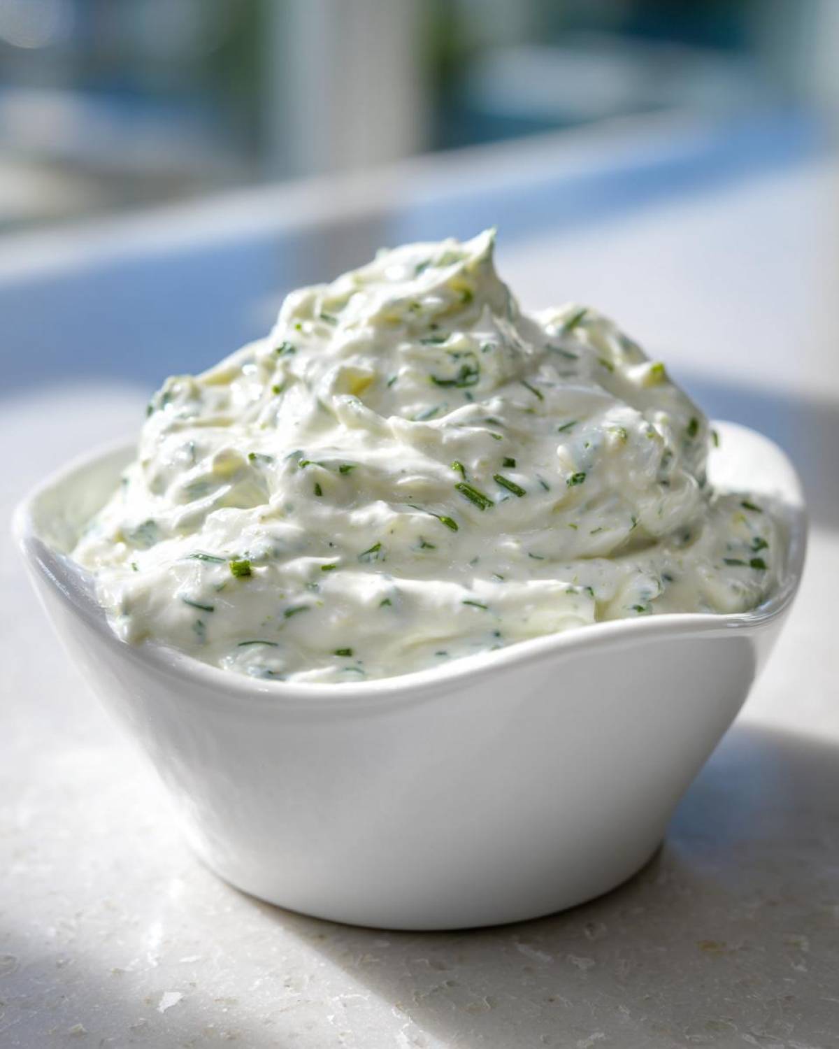 A close-up of thick, creamy 5-Minute Greek Yogurt Ranch Dip generously mounded in a small white bowl, flecked with green herbs.