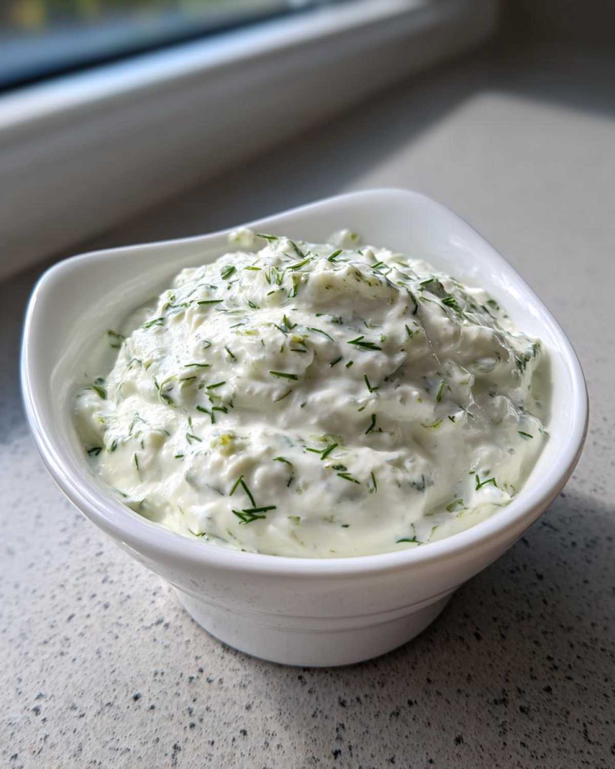 A close-up of thick, creamy 5-Minute Greek Yogurt Ranch Dip topped generously with fresh green herbs in a white bowl.