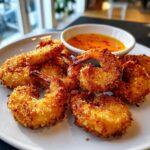Close-up of crispy, golden Air Fryer Coconut Shrimp served on a white plate with a side of sweet chili dipping sauce.