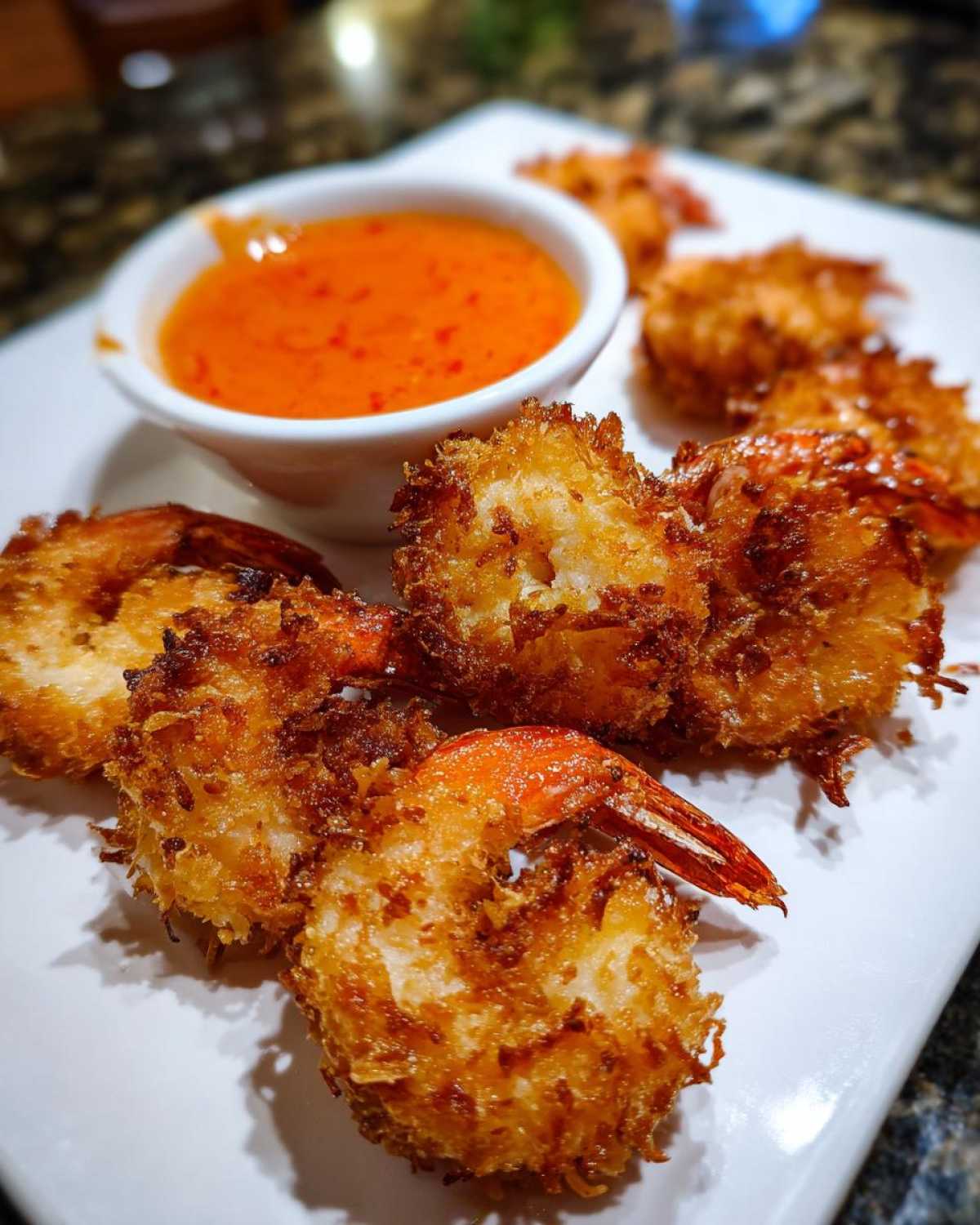 Golden brown, crispy Air Fryer Coconut Shrimp served on a white plate next to a small bowl of bright orange sweet chili sauce.