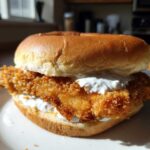 Close-up of a golden brown, crispy Air Fryer Crispy Fish Sandwich topped with white tartar sauce on a brioche bun.