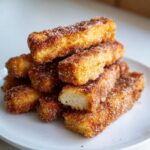 A stack of golden brown Air Fryer French Toast Sticks generously coated in cinnamon sugar on a white plate.
