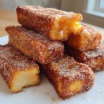 A stack of golden brown Air Fryer French Toast Sticks heavily coated in cinnamon sugar on a white plate.