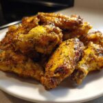 A close-up shot of a pile of golden brown, crispy Air Fryer Lemon Pepper Wings seasoned heavily with black pepper.