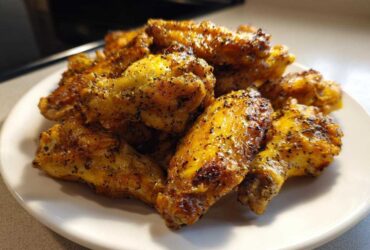 A close-up shot of a pile of golden brown, crispy Air Fryer Lemon Pepper Wings seasoned heavily with black pepper.