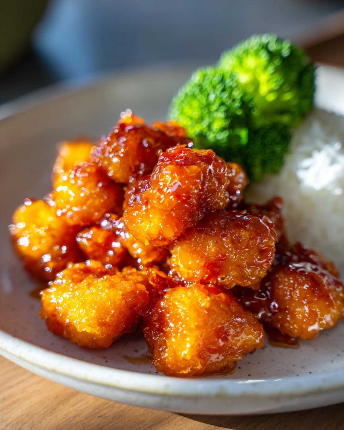 Close-up of glossy, saucy Air Fryer Orange Chicken served with white rice and steamed broccoli.