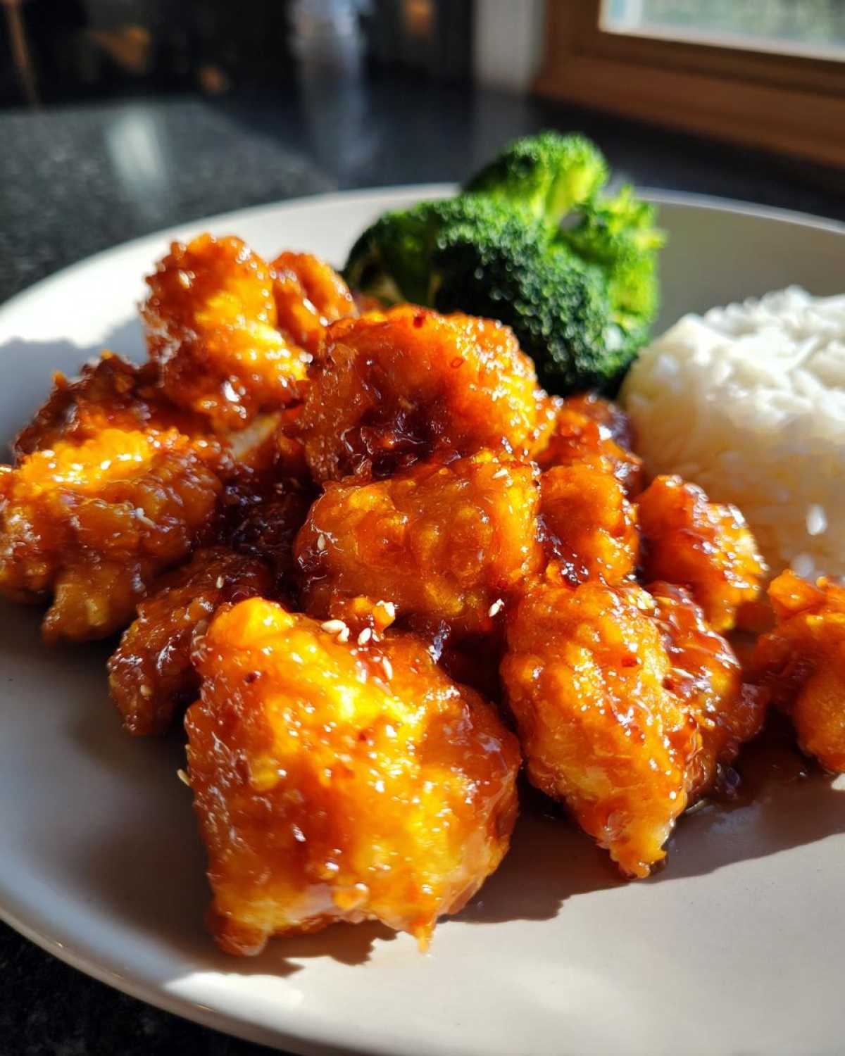 Close-up of crispy Air Fryer Orange Chicken pieces coated in a glossy sauce, served with white rice and steamed broccoli.