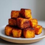 A stack of crispy, seasoned Air Fryer Sweet Potato Cubes piled high on a light-colored plate.
