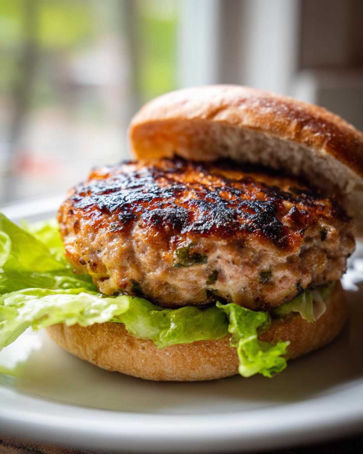 Close-up of a perfectly cooked Air Fryer Turkey Burger patty on lettuce with a toasted bun top.