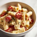 Close-up of creamy Baked Feta Pasta with Cherry Tomatoes mixed with rigatoni pasta in a white bowl.
