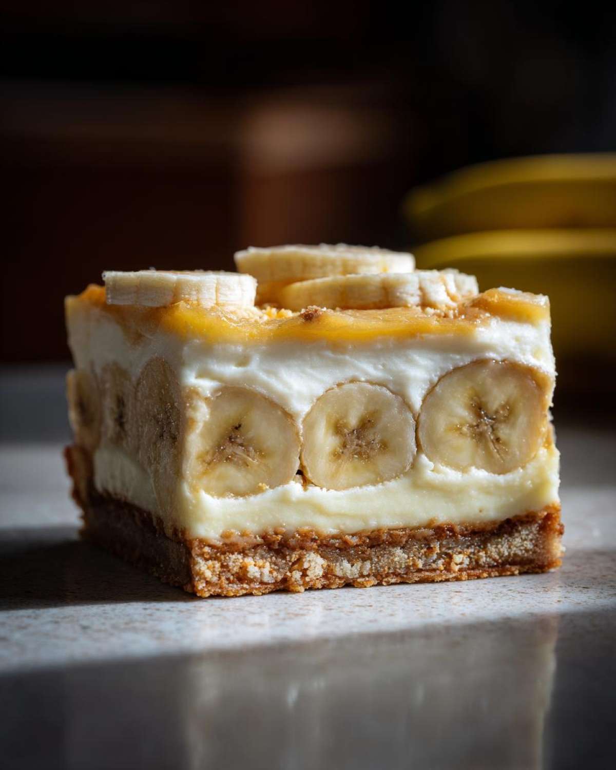 A close-up of a single serving of Banana Pudding Cheesecake Bars showing layers of graham cracker crust, creamy filling, and sliced bananas.