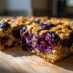 A close-up, low-angle shot of a thick slice of Blueberry Baked Oatmeal Squares showing moist interior and whole berries.