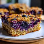 A close-up view of a thick slice of Blueberry Baked Oatmeal Squares showing the moist oat base and rich, jammy blueberry filling.