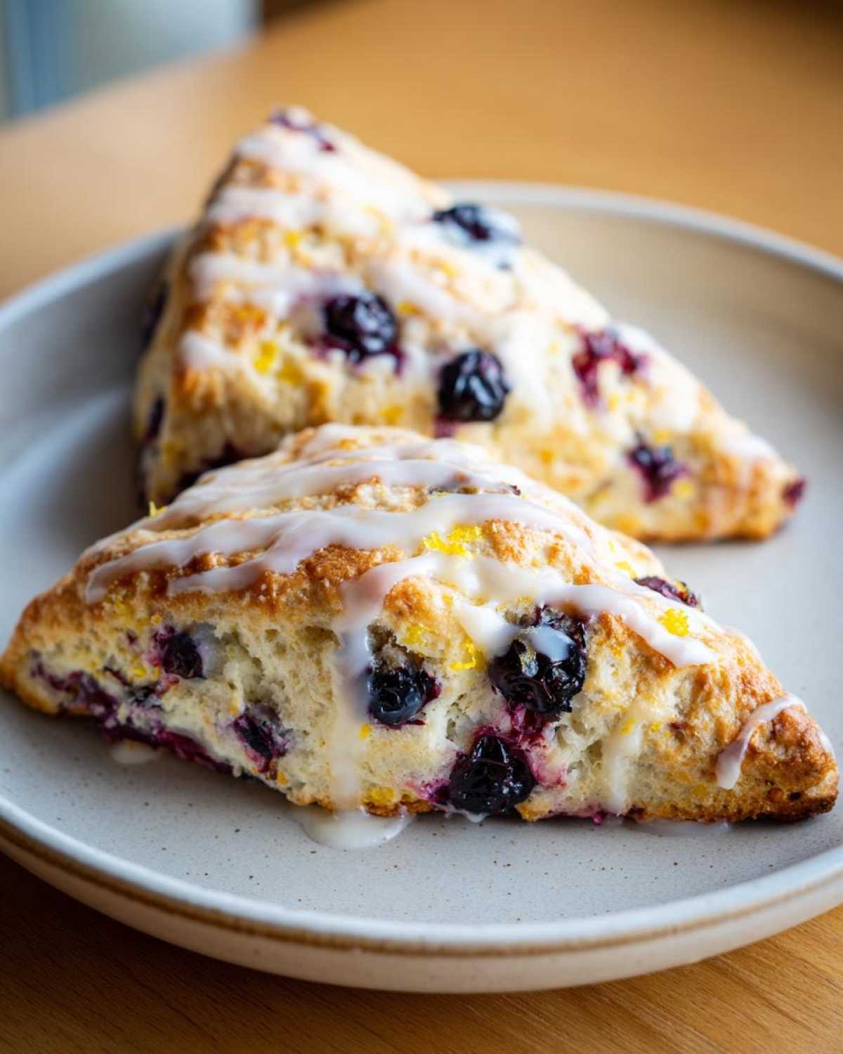 Two triangular Blueberry Lemon Scones drizzled with white glaze on a light plate.