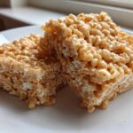 Two thick, golden-brown Brown Butter Rice Krispie Treat Bars stacked slightly on a white plate.