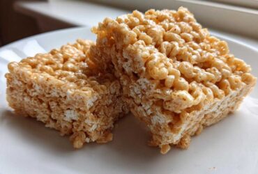 Two thick, golden-brown Brown Butter Rice Krispie Treat Bars stacked slightly on a white plate.