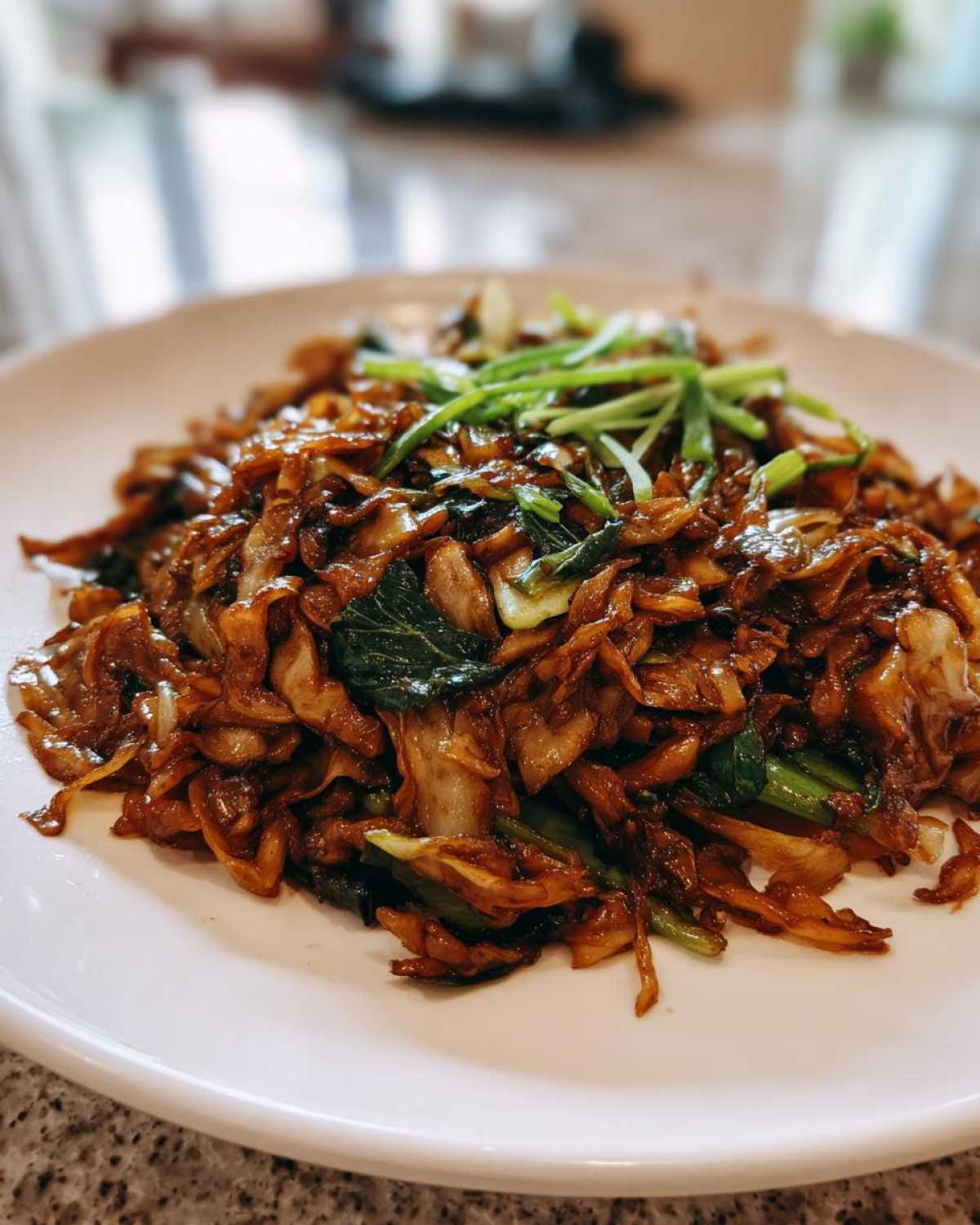 A close-up of a savory Cabbage Stir Fry with Garlic Ginger Sauce, topped with fresh scallions, served on a white plate.